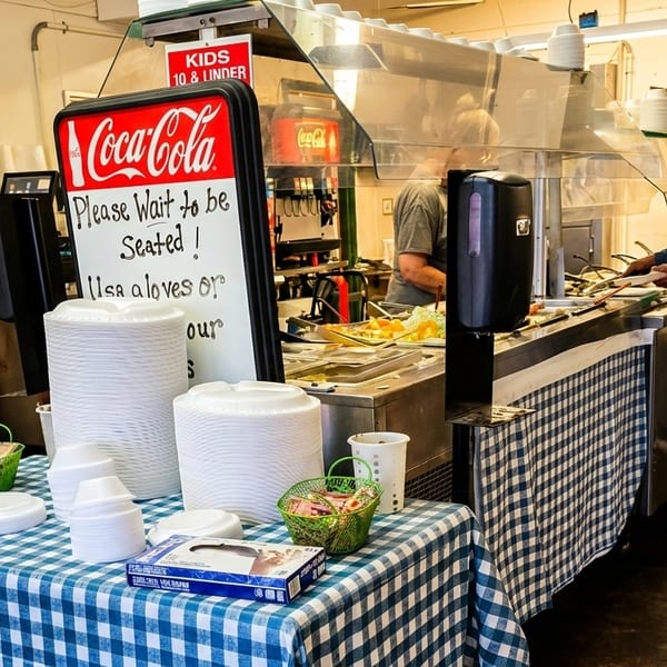 People serving themselves from a buffet line with a Coca-Cola sign and checkered tablecloth.