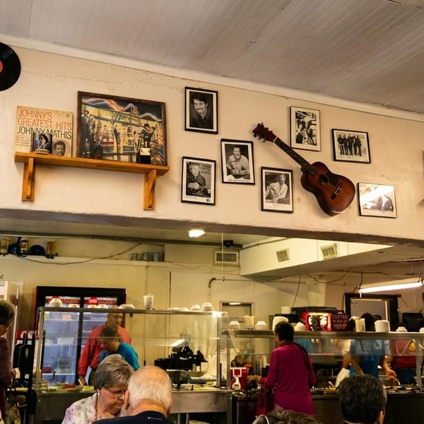 People gather at a buffet line in a casual restaurant with music memorabilia on the walls.