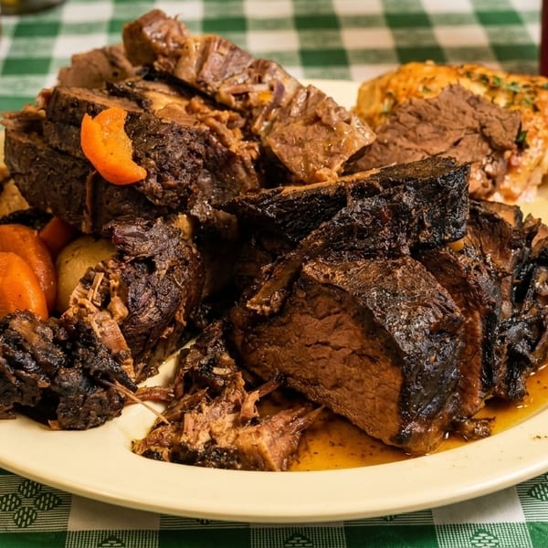 A plate of pot roast with carrots and a baked potato on a green and white checkered tablecloth.